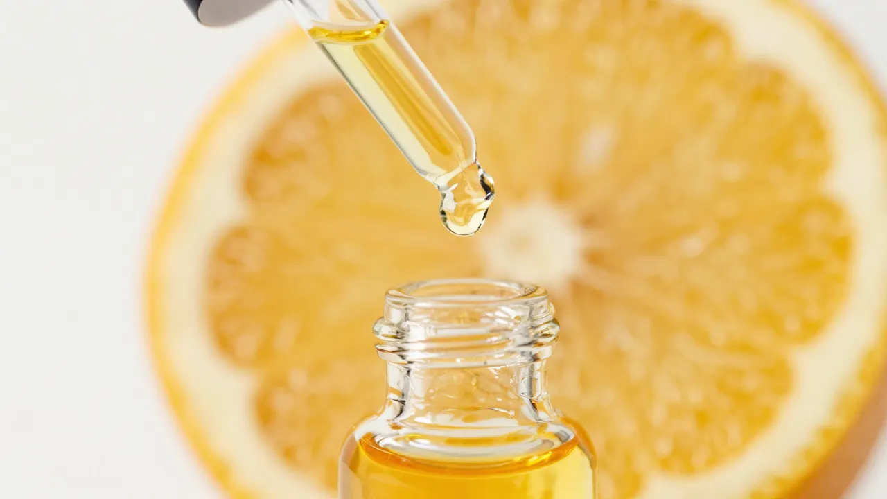 Close-up macro of golden citrus oil serum dripping from dropper with yuzu slice in background